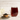 Glass of brewed Organic Pu-erh Tea with deep reddish-brown color beside a small wooden bowl filled with loose fermented tea leaves on a plate, set against a light wood background.