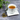 A white porcelain teacup filled with Organic Peppermint Tea on a square saucer, beside a teaspoon of loose peppermint leaves, on a textured gray surface with green foliage in the background.