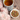 Cup of herbal tea with a patterned blue and white mug beside a bowl of loose leaf tea with rosebuds, surrounded by pink flowers on a wooden table.