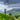 Lush green tea plantations spread across rolling hills beneath a dramatic cloudy sky.