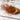 Close-up of loose Organic Rooibos Tea in a wooden spoon with scattered red-brown tea leaves on a light wooden surface.