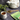 Cup of brewed Organic Tummy Balance Tea beside a white teapot with gold marbling, a bamboo spoon of loose tea blend, and a green Full Leaf Tea Co. package on a dark stone surface.
