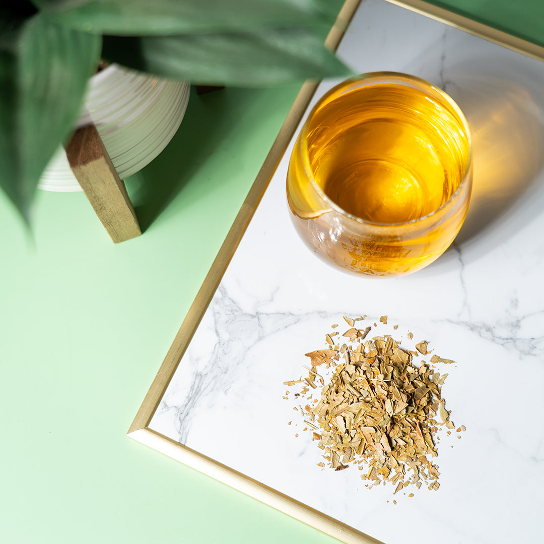 A clear glass of boldo tea with boldo leaves on a marble surface. 