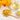 Glass of yellow tea with dried calendula flowers, a wooden spoon, and a lemon on a light surface.