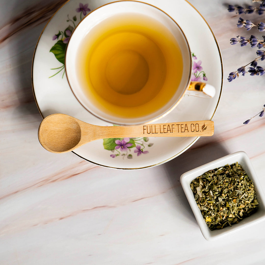 A white mug filled with catnip tea with a Full Leaf Tea Co spoon beside it and a white jar filled with catnip 