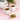 Two cups of tea with a teapot and a bowl of chickweed on a pink surface.