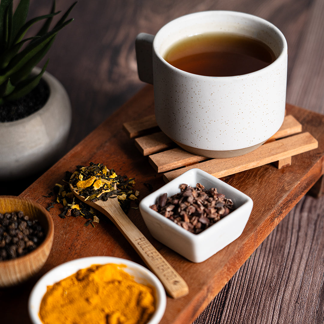 Cup of Organic Circulation Support tea on a wooden tray with turmeric powder, cacao nibs, and loose tea blend with a wooden spoon, creating a warm and earthy presentation.
