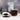 Clear glass mug filled with elderberry tea, surrounded by a bowl of black tea leaves and purple flowers on a wooden surface.