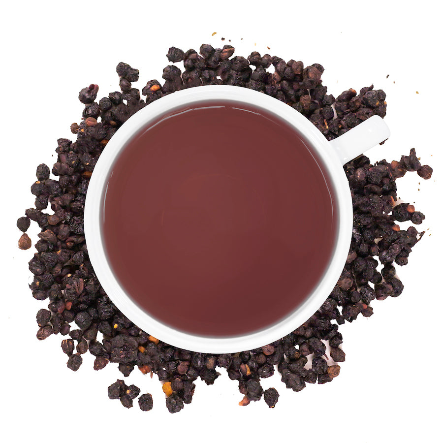 A white mug filled with Elderberry tea surrounded by elderberries on a white surface. 