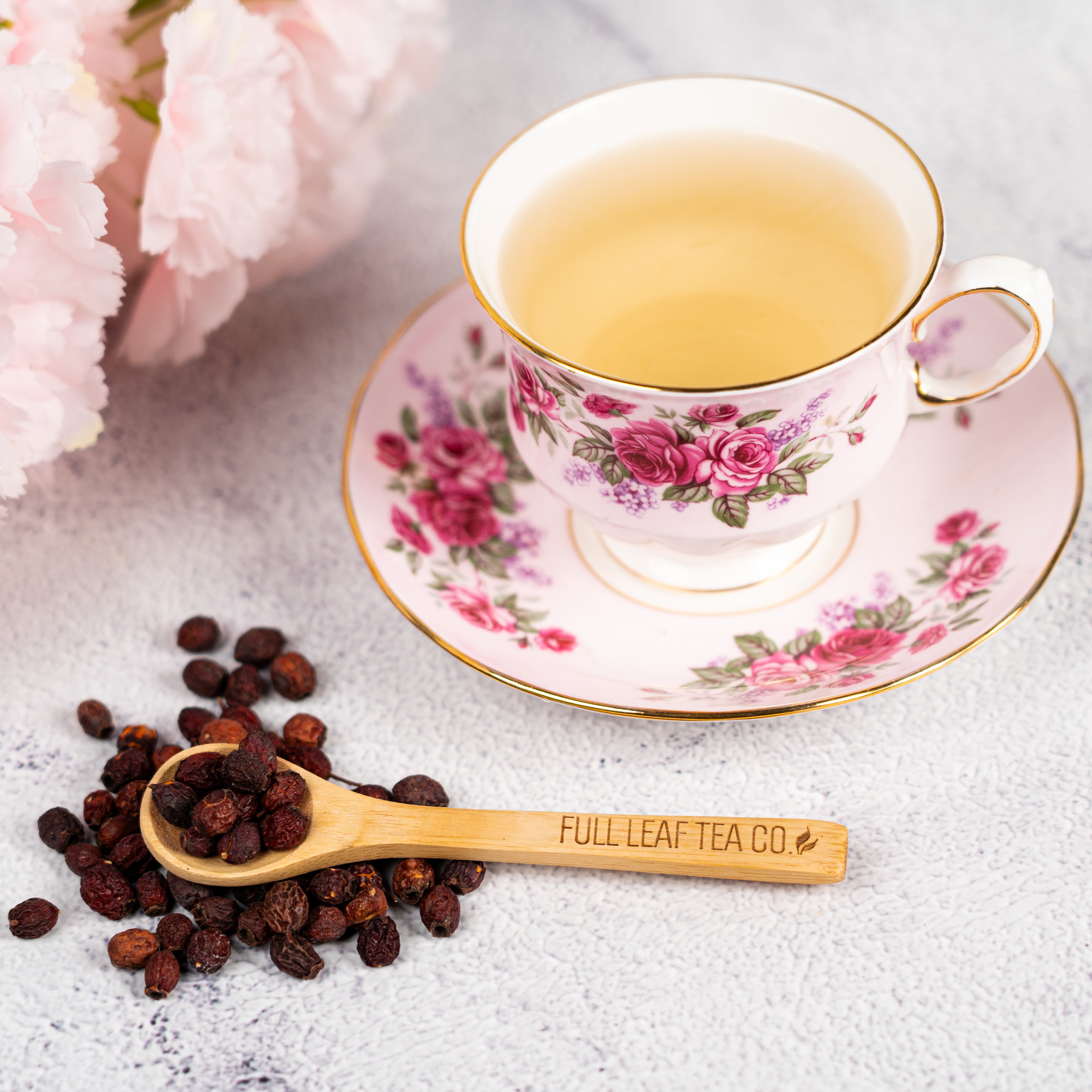 Organic Hawthorn Berry Tea in a floral pink teacup and saucer with dried hawthorn berries on a Full Leaf Tea Co. wooden spoon.