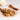Spices including cinnamon sticks and cardamom pods on a wooden spoon with a blurred floral background.