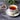 Teacup with floral design on a saucer, filled with tea, on a dark surface with lavender and heart-shaped container.