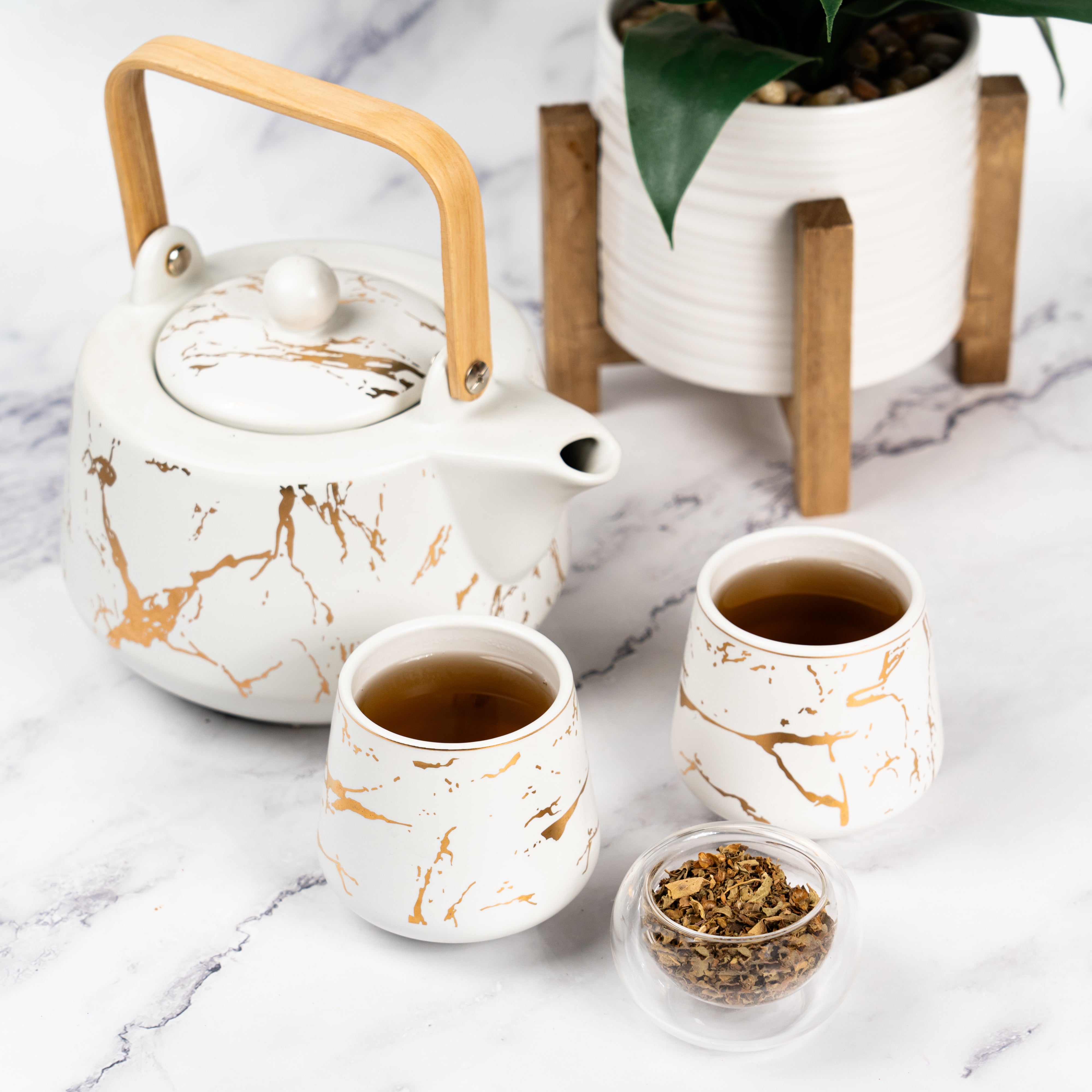 Organic Holy Basil Tea served in elegant white and gold marbled cups with matching teapot and dried holy basil leaves displayed beside it.