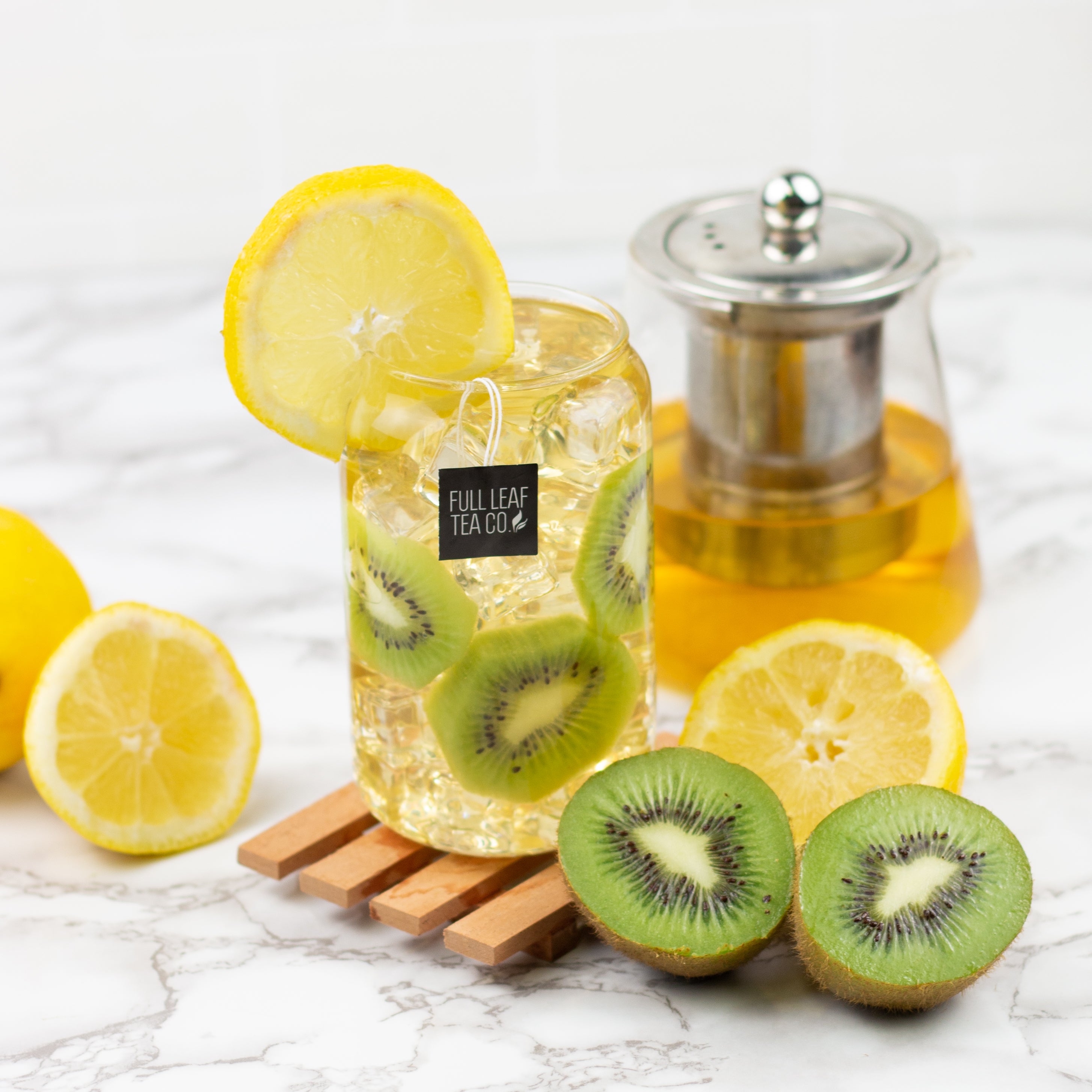 Clear glass jar with lemon and kiwi slices, labeled 'Full Leaf Tea Co', on a marble surface with lemons and kiwis.