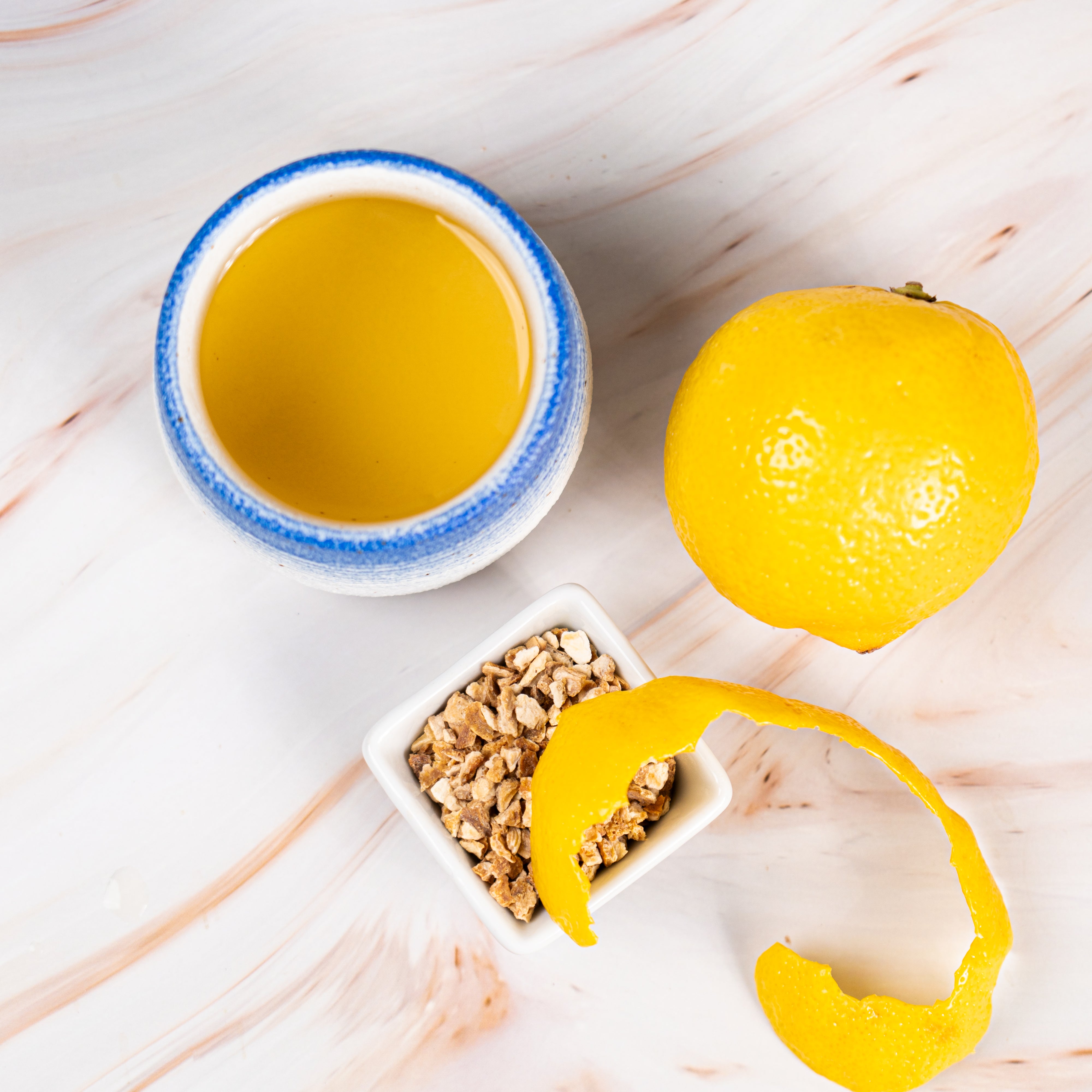 Cup of Organic Lemon Peel Tea with a whole lemon, lemon peel, and dried lemon pieces on a light marble surface.