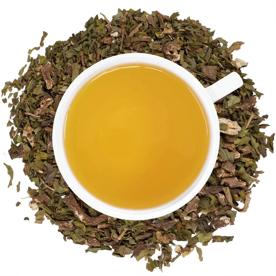 A white mug filled with dandelion tea surrounded by dandelion. 