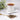 White cup of tea on a white saucer with tea leaves and a spoon on a light surface.