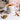 White mug with a hot beverage, cinnamon sticks, and a small bowl of honey on a marble surface.