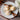 Three small cupcakes with cream cheese frosting on a white plate with cinnamon sticks and flowers on a wooden surface.