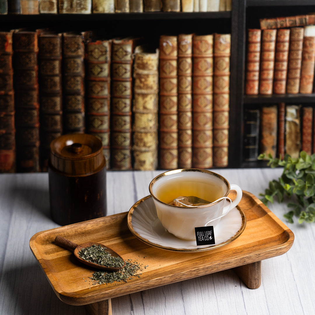 Organic wormwood tea in a cup on a wooden tray with dried herbs and vintage books in the background.