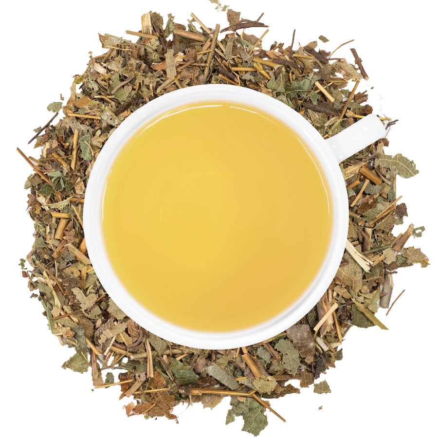 A white mug filled with epimedium tea surrounded by epimedium leaves