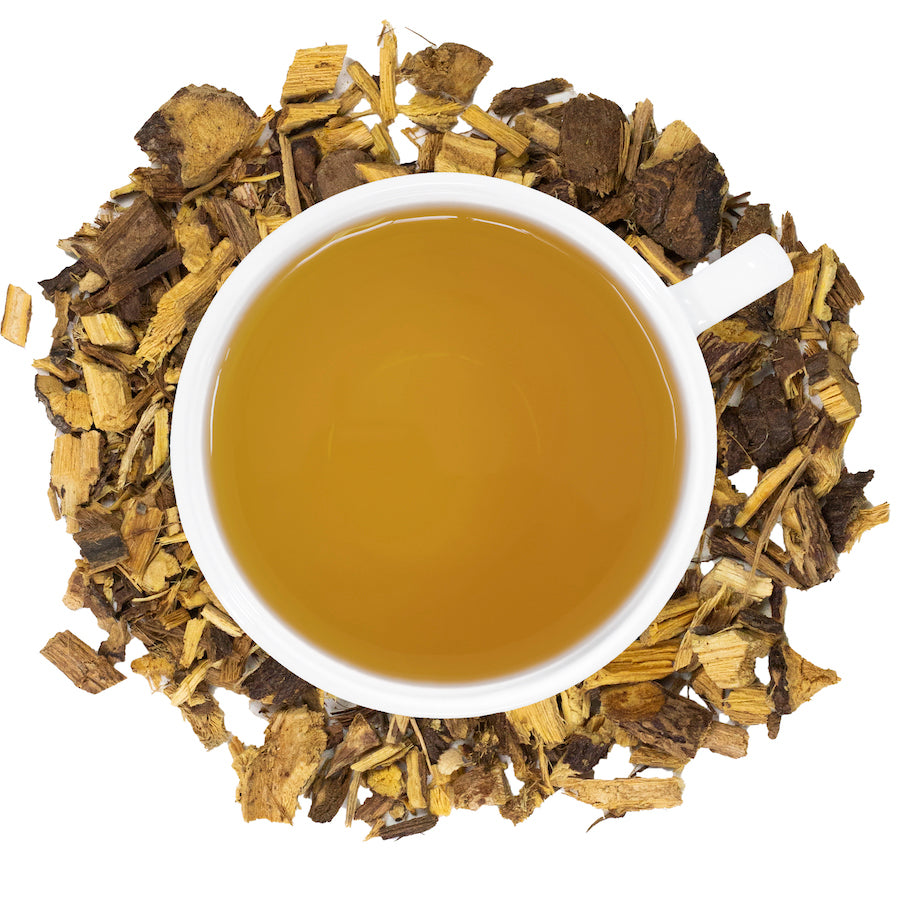 A white mug filled with licorice root tea surrounded by licorice root. 