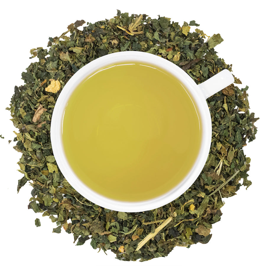 A white mug filled with Nettle tea surrounded by nettle leaves. 