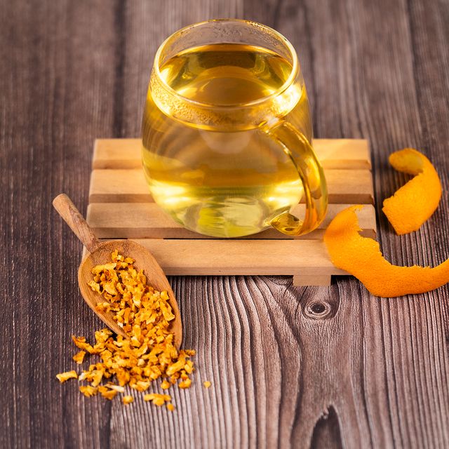 Glass cup of herbal tea with dried orange peel and zest on a wooden surface.