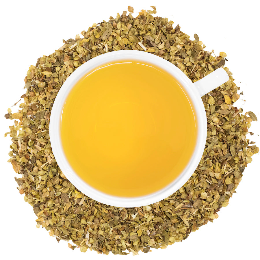 A white mug filled with oregano tea with oregano spread around the cup. 