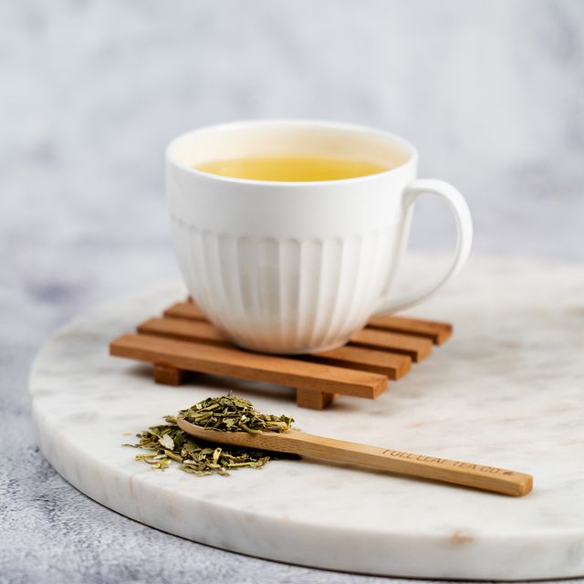 Cup of passion flower tea in a white mug on a wooden coaster, with loose passion flower tea leaves and a wooden spoon on a marble surface.