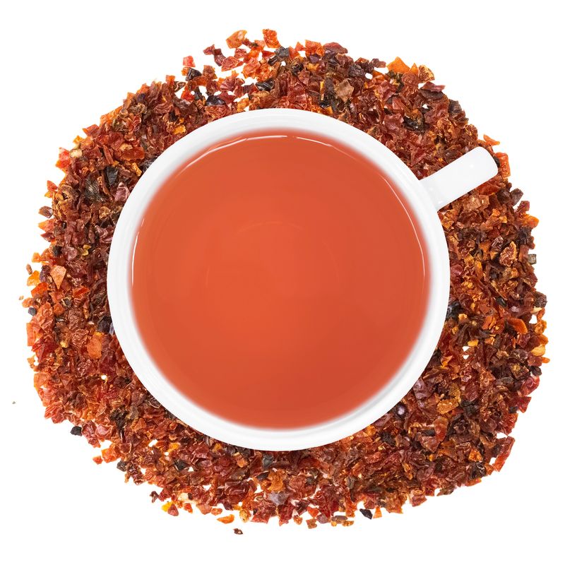 A white cup of Organic Rosehip tea, surrounded by the loose leaf tea.