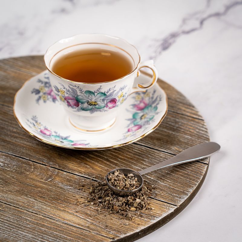 Cup of Organic Sage tea in a floral teacup on a wooden board with dried sage leaves in a spoon beside it.