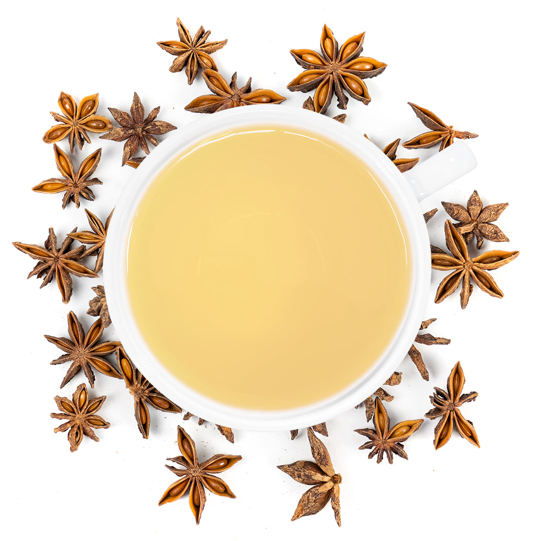 A white mug filled with star anise tea surrounded by star anise. 