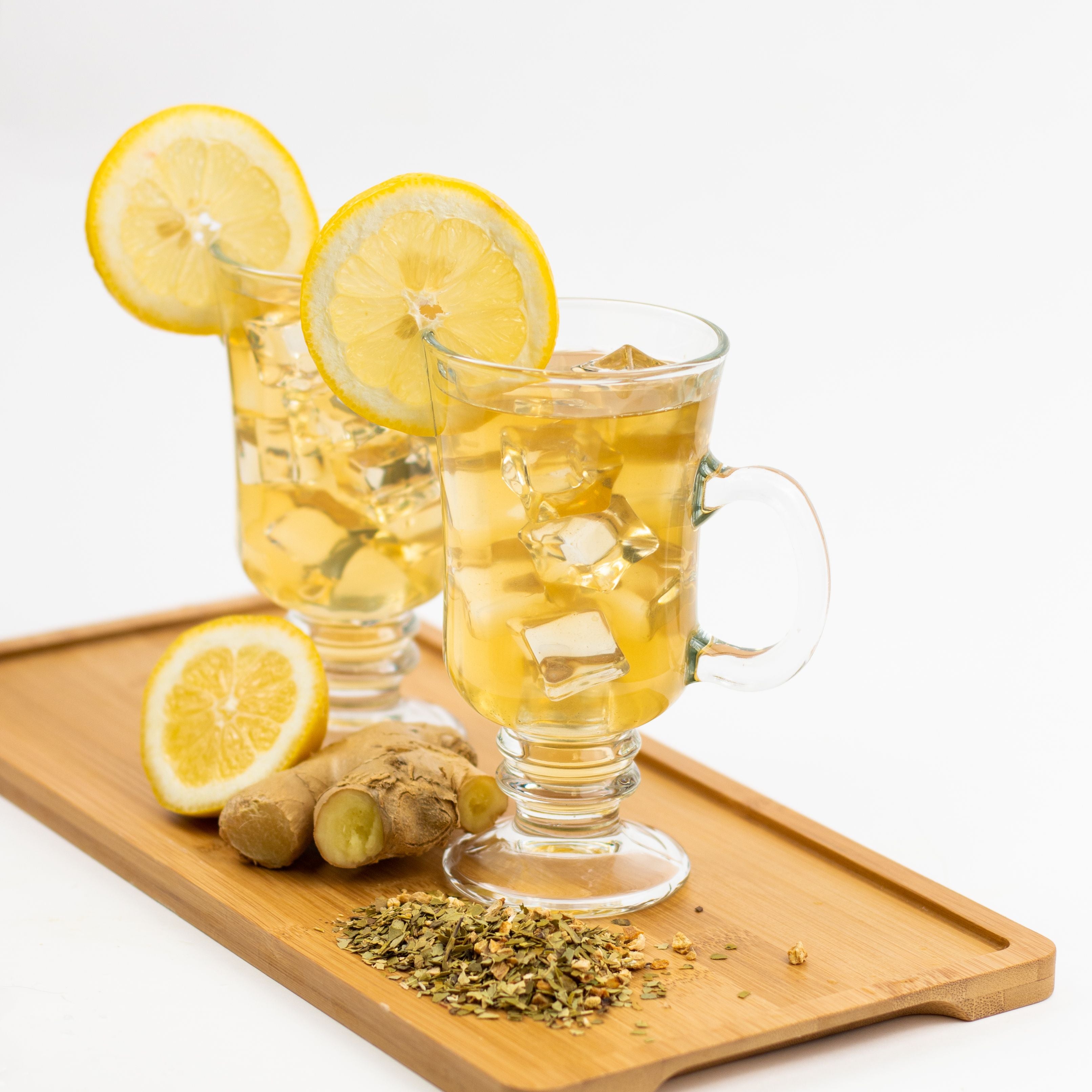Two glasses of iced tea with lemon slices on a wooden tray with ginger and tea leaves.
