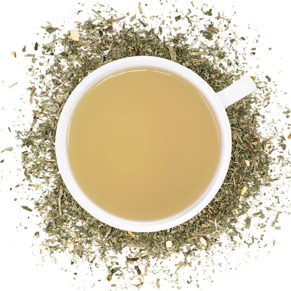 A white cup of brewed wormwood tea, surrounded by the loose leaf blend.