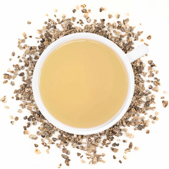 A cup of brewed Organic Devil's Claw tea with dried pieces of the root scattered around.
